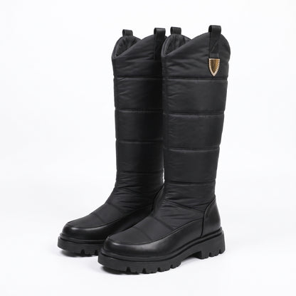 Buty zimowe damskie czarne, wysoka pikowana cholewka z ozdobną klamrą i podeszwą z bieżnikiem, na białym tle
